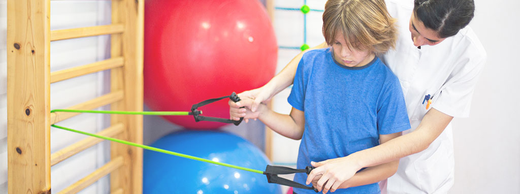 Image of a physical or occupational therapist working with resistance bands with a student and positioning the student's hands on the equipment.